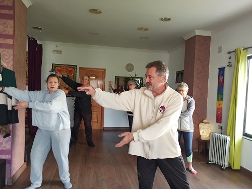 Personas adultas realizando una práctica guiada de movimiento en una sala luminosa, con un instructor en primer plano.
